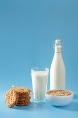 Vertical shot of milk glass, bottle, oatmeal cookies, and white bowl of oats.