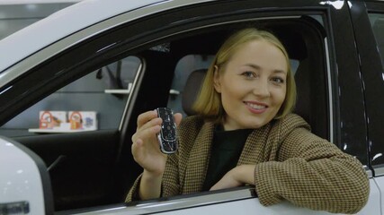 Smiling woman sitting in a new car and looking at the camera in the showroom