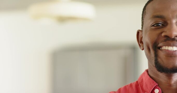 African American man in red shirt beaming at home under light fixture, blurred cabinet, copy space