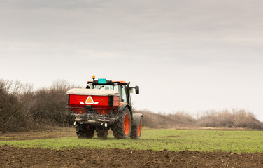 Obraz premium Tractor spreading artificial fertilizers in field