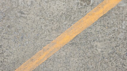 Close-up of a rough concrete surface texture with small aggregates, featuring a faded diagonal yellow line on a driveway or road.