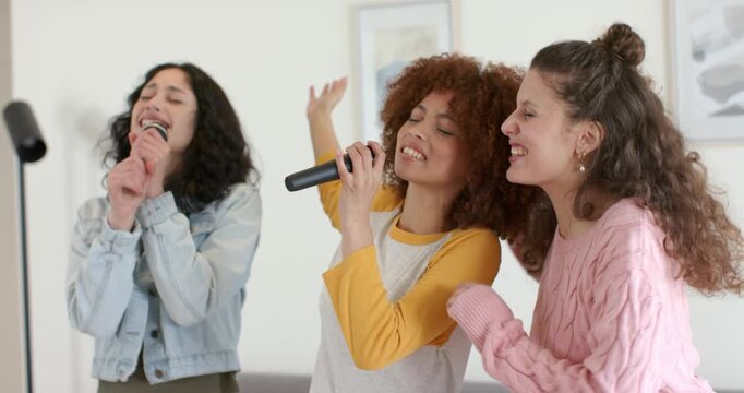 Diverse female friends singing karaoke in living room using handheld microphones, expressing unity