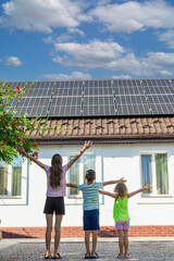 Three children with open arms standing in front of a house with solar panels