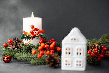 Lit white house lantern with glowing windows near green pine branch, red berries and candle