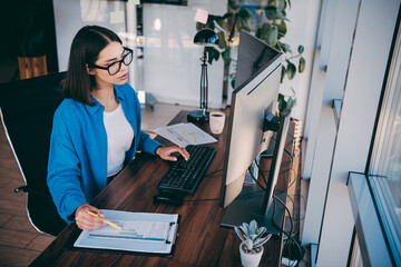 Businesswoman at a modern loft office works at a computer with clipboard notes and coffee showcasing focus and productivity