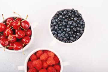 Three fruit bowls (cherries, blueberries, raspberries) on white for wellness or shared snack concept