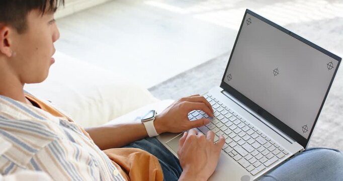 Man is placing hands on keyboard and typing on silver laptop on light couch for work