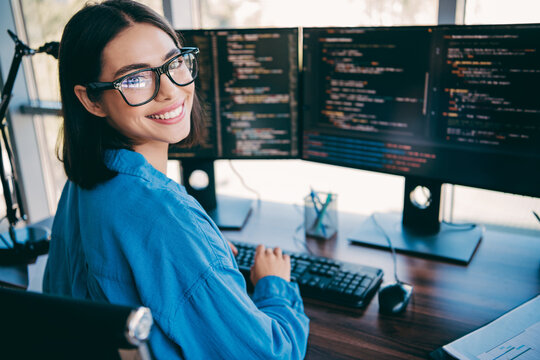 Fototapeta Female programmer at three monitors smiling while coding in modern office setting