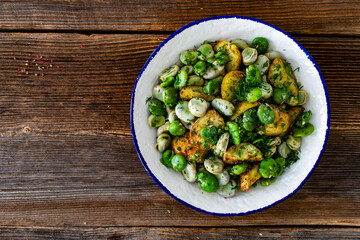 Boiled broad bean with baked potatoes in bowl on wooden table

