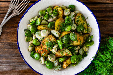 Boiled broad bean with baked potatoes in bowl on wooden table
