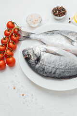 Close up of two dorado fish on white plate with lemon and tomato