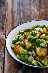 Boiled broad bean with baked potatoes in bowl on wooden table
