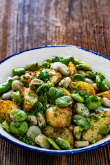 Boiled broad bean with baked potatoes in bowl on wooden table
