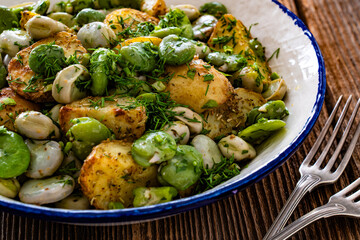 Boiled broad bean with baked potatoes in bowl on wooden table
