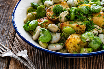 Boiled broad bean with baked potatoes in bowl on wooden table
