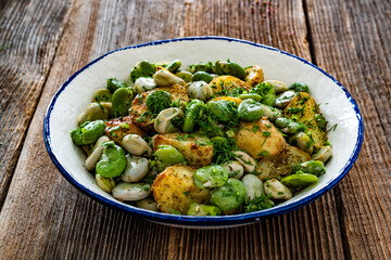 Boiled broad bean with baked potatoes in bowl on wooden table
