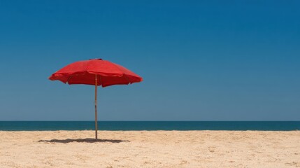 Red umbrella stands alone on sandy beach by the ocean under clear sky