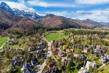 Aerial panoramic view of the Strążyska Valley near Zakopane, Poland, showcasing the distinctive Giewont mountain peak and residential areas surrounded by lush green forests in the Tatra Mountains.