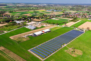 Renewable energy source. Aerial panorama of a massive solar PV power plant installation surrounded by lush green fields in a rural setting, symbolizing technology and sustainability.