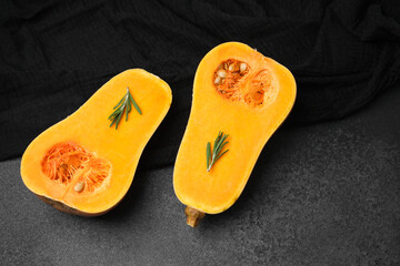 Two halved butternut squash with rosemary sprigs on a dark surface with a black cloth