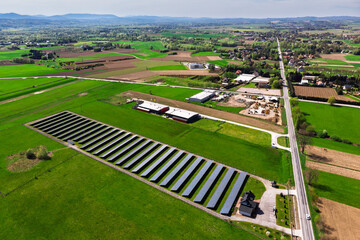 Renewable energy source. Aerial panorama of a massive solar PV power plant installation surrounded by lush green fields in a rural setting, symbolizing technology and sustainability.