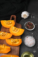 Sliced orange pumpkin pieces on wooden board with garlic, peppercorns, and salt
