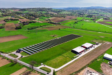 Renewable energy source. Aerial panorama of a massive solar PV power plant installation surrounded by lush green fields in a rural setting, symbolizing technology and sustainability.