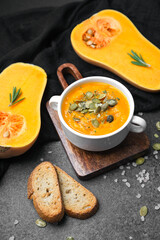 Warm pumpkin soup in bowl with toasted bread and herbs on dark background