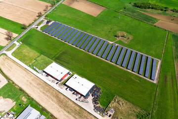 Renewable energy source. Aerial panorama of a massive solar PV power plant installation surrounded by lush green fields in a rural setting, symbolizing technology and sustainability.