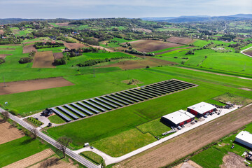 Renewable energy source. Aerial panorama of a massive solar PV power plant installation surrounded by lush green fields in a rural setting, symbolizing technology and sustainability.