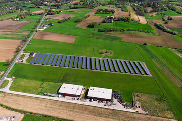 Renewable energy source. Aerial panorama of a massive solar PV power plant installation surrounded by lush green fields in a rural setting, symbolizing technology and sustainability.