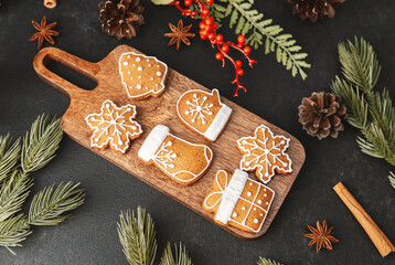 Gingerbread cookies with festive icing on a wooden board with pine cones and evergreen branches