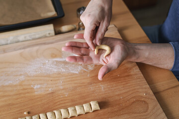 Ein Mann formt Vanillekipferl Kekse in seiner Hand. Zuhause, Weihnachten. 