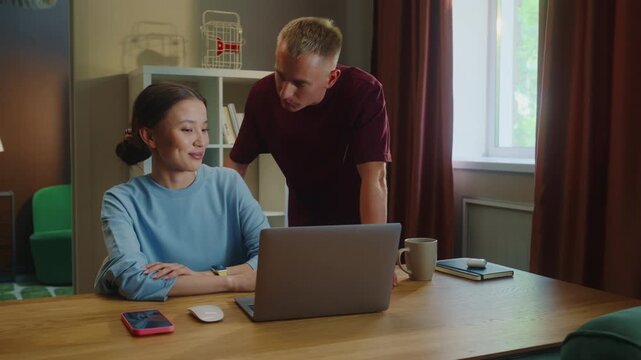 Boss man checks asian woman subordinate do task correctly report. Management satisfied work. Employee right answer. Good job. Guy show laptop screen. Multi racial national couple online shopping home.