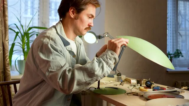 Craftsman assembling vintage item, checking condition of old lamp, evaluates lampshade fixation, bottom base mount, broken switching button, thinks about transformation, what materials or tools to use