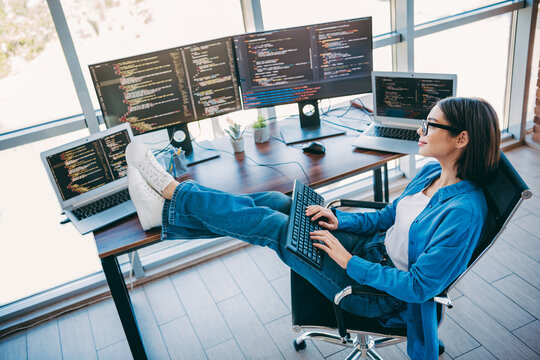 Female programmer in a modern loft office working with multiple screens and laptop focused on coding and project work in a professional tech setting - Powered by Adobe