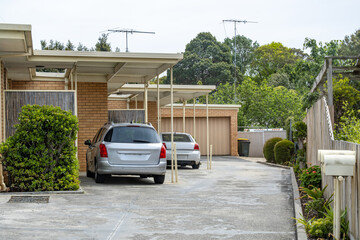 Suburban townhouse driveway with covered carports and parked vehicles beside brick residential units in Australia. Concept of parking, shared access driveway, and private vehicle storage