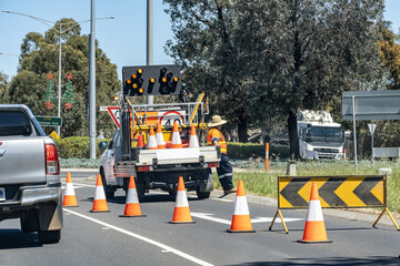 Road maintenance crew setting up traffic control with safety cones, arrow board, and work vehicle...