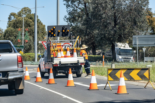 Fototapeta Road maintenance crew setting up traffic control with safety cones, arrow board, and work vehicle on a suburban street in Australia. Concept of roadworks, temporary traffic management