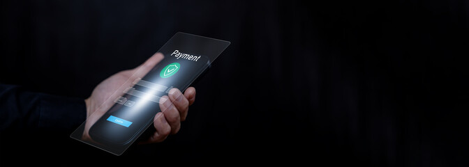 Hand holding a smartphone with a futuristic transparent payment interface, featuring dark background copy space for adding text. Concept of secure mobile payment and fintech innovation.