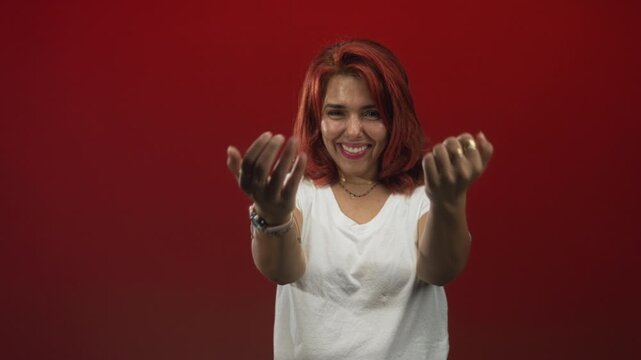 Woman pointing both hands forward with visible hands and a bright smile in studio red; confidence invitation welcome.