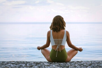 Woman meditating on a pebble beach by the ocean