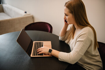 Busy business trader talking on phone. Young stressed analyst woman looking at laptop monitor, feeling tired frustrated reading bad news on financial market working in home office. Trading online.