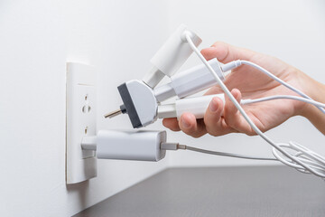 Hand inserting electrical plugs into outlet. Electrical overload