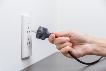 Female hand inserting a black electrical plug into outlet