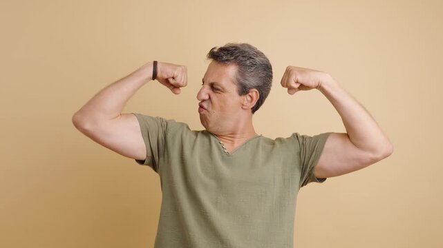 Playful mature man flexing his biceps and making a series of funny, silly faces for the camera against a simple beige background