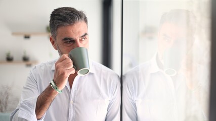 Mature man drinking coffee looking pensive by window