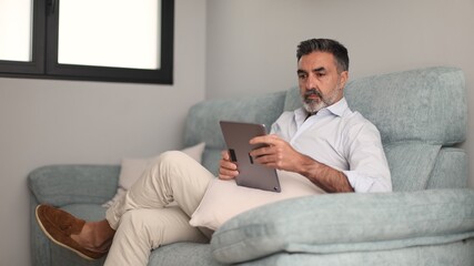 Mature man relaxing on couch using tablet