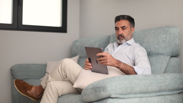 Mature man relaxing on couch using tablet - Powered by Adobe