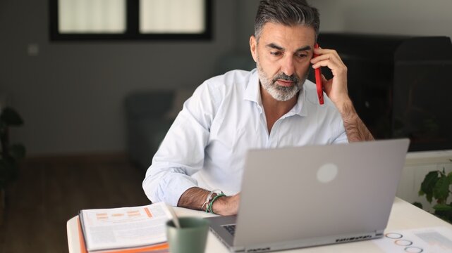 Busy businessman working remotely with laptop and phone call - Powered by Adobe